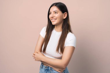 Beyaz gömlekli ışıl ışıl genç bir kadın, kolları çaprazlanmış ve saçları kulağının arkasına sıkışmış, kendine güven ve neşe saçan. Yaşam tarzı, güven ve modern moda temaları için ideal.