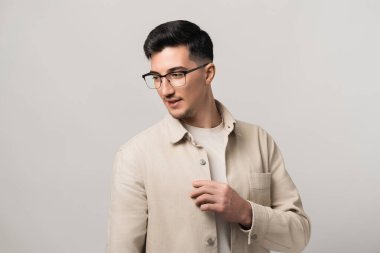 Gözlüklü, açık bej ceketli yakışıklı esmer adam samimi poz veriyor, modern ve otantik kulaklıkları takıyor..