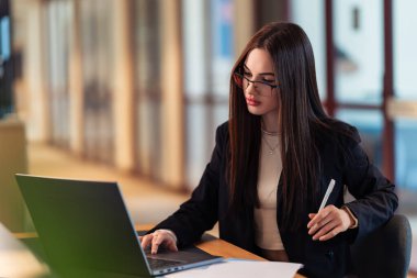 Odaklanmış, azimli, durdurulamaz. Modern bir ofiste dizüstü bilgisayarı üzerinde çalışan profesyonel bir kadın görevlerini özgüvenle yerine getiriyor. Hızlı çalışma ortamında verimlilik ve hırs..
