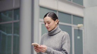 Hareket halinde, her zaman çevrim içi. Şehre yakın şık ofislerde dolaşan bir kadın, yürürken telefonunu kullanıyor, teknoloji ve hızlı yaşam tarzını dengeliyor..