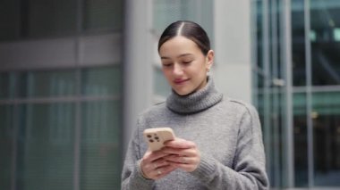 Sabah yürüyüşü, hareket halindeki mesajlar. Rahat bir kıyafet giymiş bir kadın cam mimarisinin önünden geçiyor, telefon elinde, hayatı her adımda yaşıyor..