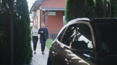 Genç ve güzel bir çift. Bir adam ve bir kadın evlerinin otoparkındalar. Arabalarına biniyorlar. Karı koca gülümser ve birbirleriyle konuşurlar. Adam kadının arabaya binmesine yardım eder..