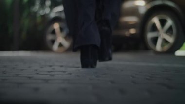 Kamera kadın bacaklarının yakın çekimini gösteriyor. Yüksek topuklu ayakkabı giyiyor ve arabasına yaklaşıyor. - Kadın arabaya biniyor. Kamera hala yerde duruyor..