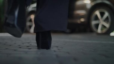 Kamera yerde, bize aşağıdan manzarayı gösteriyor. Bir kadın bacağının yakın çekimini görüyoruz. Yüksek topuklu ayakkabı giyiyor ve arabasına biniyor. Kamera yerde kalıyor..