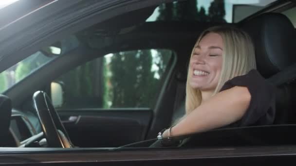 美しい女性が運転席にいる 彼女は窓を開けて微笑んだ 女の子はハンドルを握りながらカメラをポーズした 女の子は陽気な気分だ — ストック動画