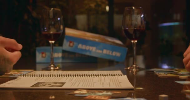 ワインのメガネが2つあり ボードゲームのルール付きのノートブック そこからボックスがあります スクリーンにハンドが現れ サイコロを振ります テーブルの上に落ちるサイコロのゆっくりとした動きが見られます — ストック動画