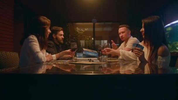 4人の友人がボードゲームをしています テーブルには男と女が二人いる 二人の男が試合について議論している 女性の一人がサイコロを投げる 別の女性が彼女のワインのグラスに触れる — ストック動画