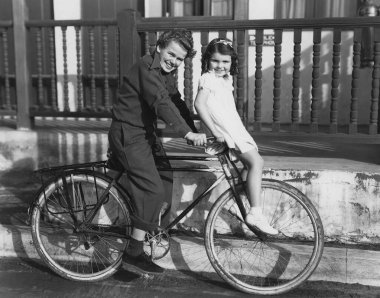 Güneşli bir günde bisiklet üzerinde oturan gülümseyen erkek ve kız kardeşlerin tam boy yan görünüm portresi 