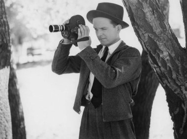 Film yapımcısı ağaçta dururken kamerayla çekim yapıyor.  