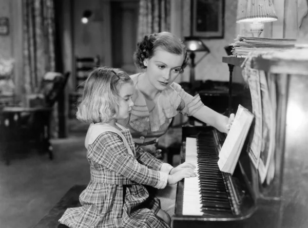 Young female pianist looking at sheet music while teaching girl at home