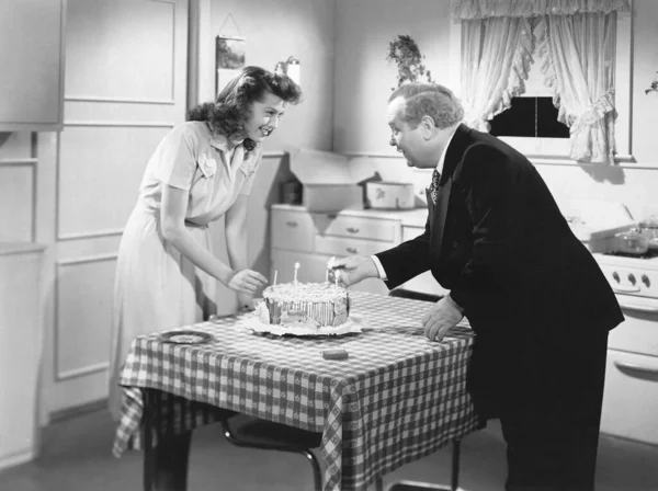 Two people prep a birthday cake in the kitchen.