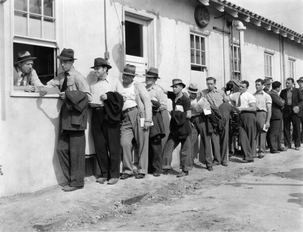 Работники мужского пола стоят в очереди у здания фабрики в солнечный день 