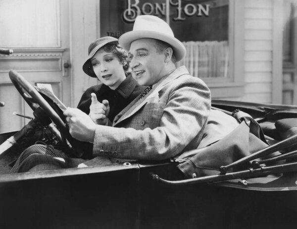 Happy couple sitting in car while reading paper on sunny day 