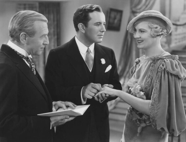 Minister watching groom putting ring on bride's finger at church