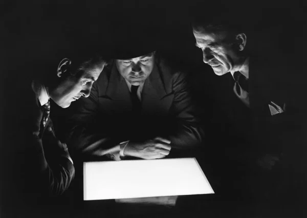 Neugierige Männer Blicken Dunkeln Auf Beleuchtetes Licht lizenzfreie Stockbilder