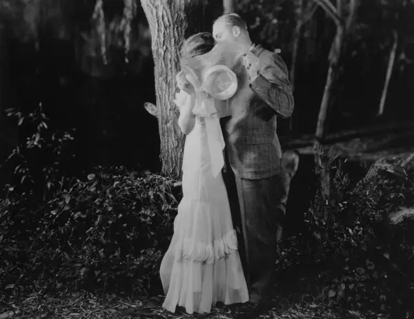 夜の公園の木に対して帽子の後ろにキスするカップルの完全な長さの側面の眺め — ストック写真