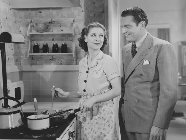 自宅でキッチンで食べ物を準備している女性を見ている笑顔の男 ストック画像