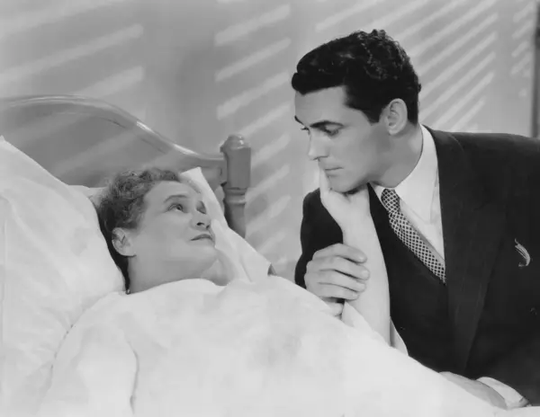 ベッドに横たわっている病気のシニアマザーを見ている心配な若者 ストック写真