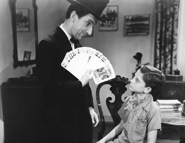 魔术师用扑克牌向男孩表演把戏 图库照片