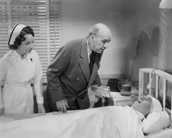 心配した医師と看護師が病院のベッドに横たわる男性患者をチェック ストックフォト