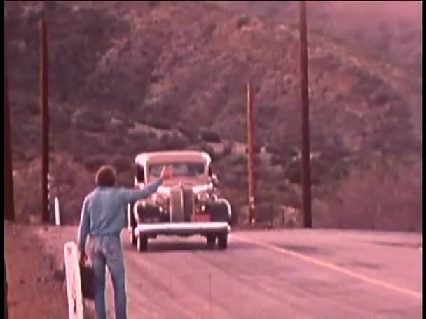 1970 年代の田舎道でヒッチハイクのブリーフケースを持った男の後姿 — ストック動画