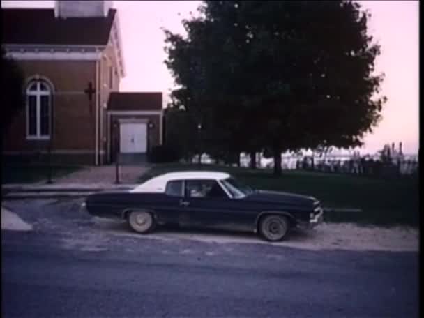 Man Kör Vintage Bil Landsväg Med Kyrka Och Kyrkogård 1980 — Stockvideo