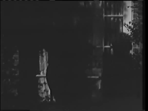 1940 年代の窓から家に入るフード男の後姿 — ストック動画