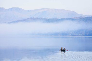 LAKE DISTRICT, UK - October 12, 2010. Couple paddling a double canoe on a lake, misty morning in autumn. Coniston Water, Lake District, England, UK