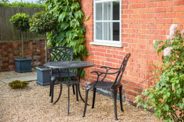 Landscaped garden design with bistro table and chairs on gravel in traditional UK garden