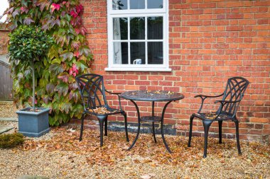 Bahçe bahçe mobilyalarıyla sonbaharda sert manzaralı bir bahçe. Siyah metal bistro masası ve sandalyeli çakıllar..