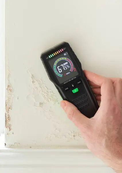 stock image Moisture detector (moisture testing meter) against a wall with rising damp, reading high moisture content. UK home interior