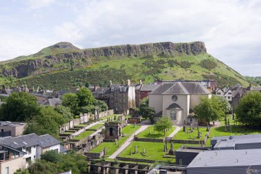 Arka planda Salisbury Kayalıkları ve Arthur Koltuğu olan Kirk ve mezarlığı canlandırın. Edinburgh, İngiltere