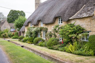 Cotswolds U 'daki Oxfordshire köyünde, Minster Lovell' da taştan duvarları ve yemyeşil bahçeleri olan geleneksel sazdan bir kulübe.