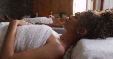 Havlu giymiş, gözleri kaplıcada masaj masalarına kapalı yatan rahat çiftlerin videosu. Tatil, birliktelik, rahatlama, sağlık, mutluluk ve kapsayıcılık kavramı.