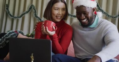 Noel Baba şapkalı mutlu çiftin videosu. Gülümsüyor ve evde dizüstü bilgisayar kullanıyorlar. Noel, kutlama, iletişim, mutluluk ve kapsayıcılık kavramı.