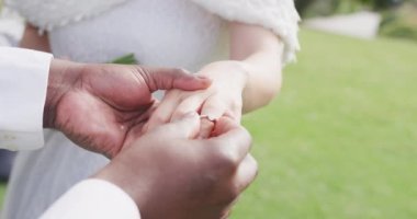 Farklı gelin ve damat elleri, damat açık hava düğününde gelinin parmağına yüzük takıyor. Evlilik, aşk, mutluluk ve kapsayıcılık kavramı.