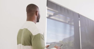 Mutlu Afro-Amerikan bir adamın gülümsediği, tabletle ayakta dikildiği bir video. Ev hayatı, iletişim, sağlık, mutluluk ve kapsayıcılık kavramı.