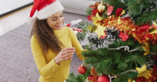Video Feliz Mujer Biracial Sombrero Santa Sonriendo Decorando Árbol Navidad — Vídeos de Stock