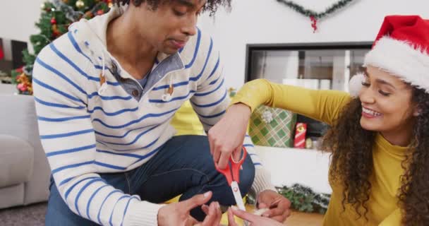 家庭でクリスマスプレゼントを包んだ幸せな多様なカップルのビデオ クリスマス お祝い 伝統と包括的な概念 — ストック動画