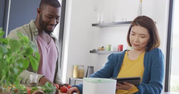 食事を準備し タブレットを使用し キッチンで野菜を堆肥化する幸せな多様なカップルのビデオ 国内生活 コミュニケーション 幸福と包括的な概念 — ストック動画