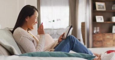 Tabletle koltukta dinlenen mutlu Asyalı kadının videosu. Boş zaman, rahatlama, evde teknoloji konseptiyle zaman geçirme..