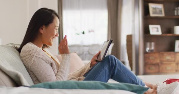 幸せなアジア人女性の動画がタブレットでソファに休んでいます レジャー リラックス テクノロジーのコンセプトで自宅で時間を過ごす — ストック動画