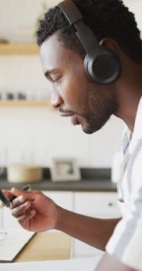 Mutfaktaki masada oturup video bloğu yapan mutlu Afro-Amerikan bir adamın dikey videosu. Evde yalnız zaman geçirmek..