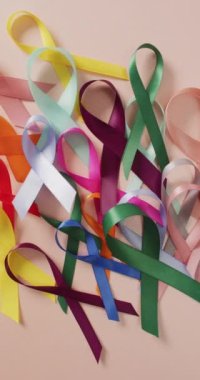 Pembe arka planda renkli kurdelelerin dikey videosu. Sağlık, önleme, ilaç, semboller ve kanser farkındalığı kavramı.