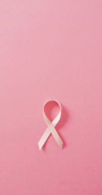 Pembe arka planda pembe kurdelenin dikey videosu. Sağlık, önleme, ilaç, semboller ve kanser farkındalığı kavramı.