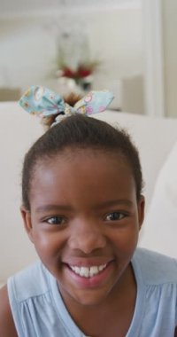 Afro-Amerikan mutlu bir kızın oturma odasında gülüşünün dikey video portresi. çocukluk yaşam tarzı, bedensel bütünlük, evde kaliteli zaman geçirmek..