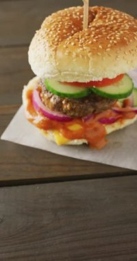 Tahta arka planda salatalı taze ev yapımı hamburgerin dikey videosu. Taze ev yapımı fast food..