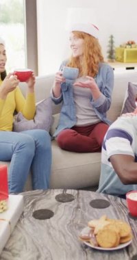 Çeşitli mutlu arkadaşların evde sıcak çikolata içerek Noel 'i kutladıklarının dikey videosu. Noel, kutlama, gelenek, arkadaşlık, kapsayıcılık ve yaşam tarzı konsepti.