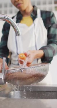 Afro-Amerikan kadının sebze yıkarkenki dikey videosu. Yaşam tarzı ve ev kavramında zaman geçirme.