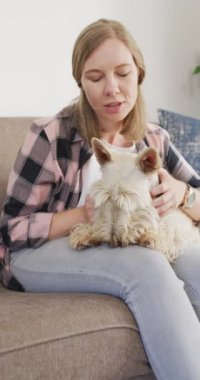 Evinde köpeğini okşayan mutlu beyaz kadının dikey videosu. Evde birlikte vakit geçirmek..